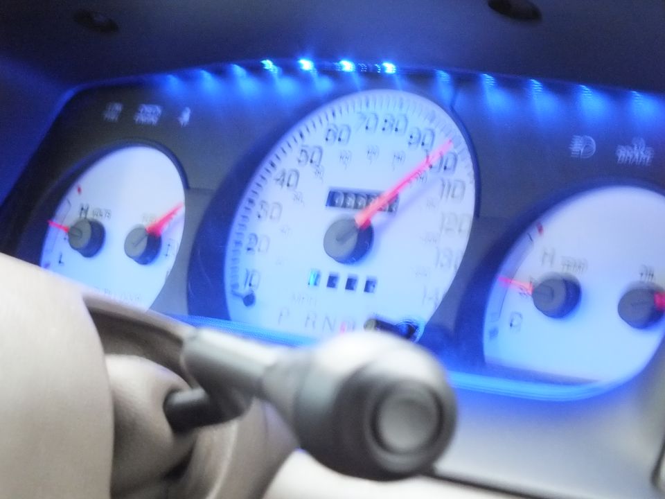 Blurred blue-lit speedometer gauge cluster with red needles and PRND indicators