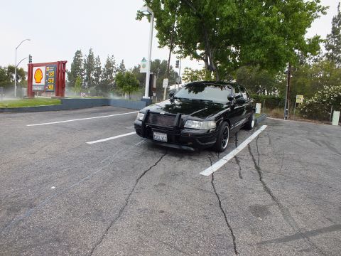 2003 Ford Crown Victoria - Lowered black sedan with brush guard in a cracked parking lot beside a Shell gas sign.
