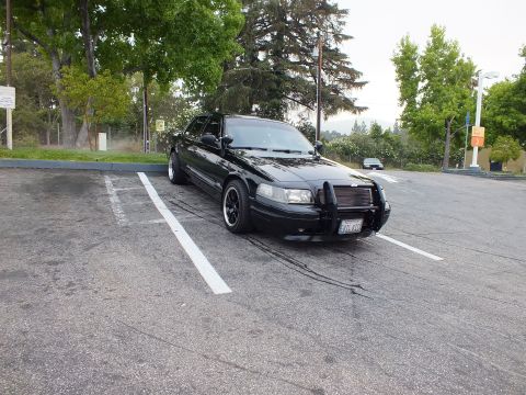 2003 Ford Crown Victoria - Lowered black Crown Victoria sedan angled in an empty lot, push bar mounted on the front.