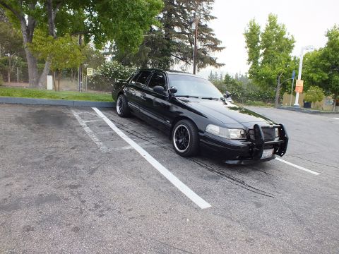 2003 Ford Crown Victoria - Side view of a lowered black full-size sedan with dark wheels, parked across painted lot lines.