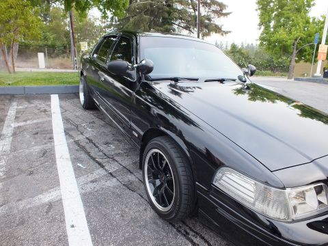 2003 Ford Crown Victoria - Close front-quarter shot of a glossy black sedan riding low on black wheels in a parking lot.