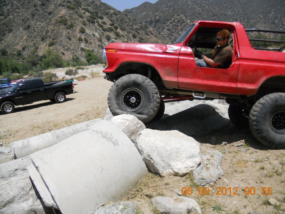 Red off-road truck with big tires navigating rocks. Black pickup truck in background