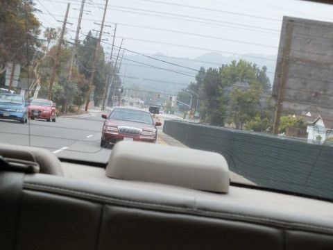 2003 Ford Crown Victoria - View through a car rear window of a maroon Lincoln sedan on a hilly street with power lines.