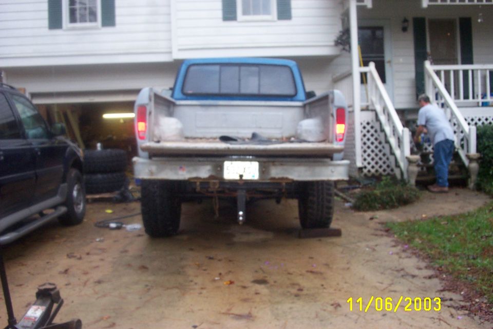 Rear view of a lifted blue and white Ford pickup with tailgate down in a driveway