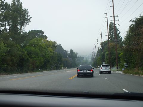 2003 Ford Crown Victoria - Windshield view of a black sedan and a white SUV driving a divided road toward mist-covered hills.