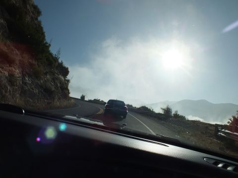 2003 Ford Crown Victoria - Backlit dark vehicle rounding a curve on a mountain road, sun flaring above haze in the valley.