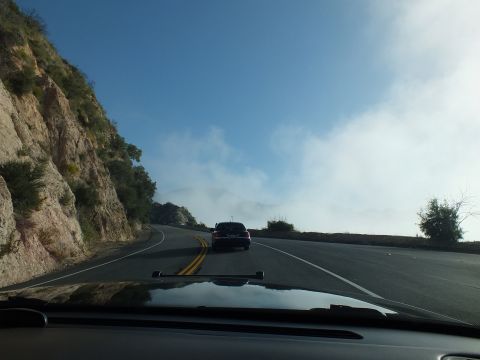 2003 Ford Crown Victoria - Windshield view of a dark sedan on a sweeping mountain highway curve next to a steep rock cut.
