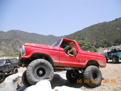 1986 Ford Bronco - Red Ford Bronco navigates rocky terrain with a driver behind the wheel.
