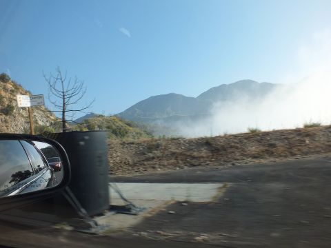 2003 Ford Crown Victoria - Out-the-window shot of a roadside pullout, dust rising over scrub with mountain ridges beyond.