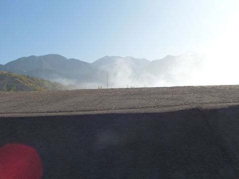 2003 Ford Crown Victoria - Layered mountain peaks rise behind a graded dirt slope, soft haze drifting across the range.