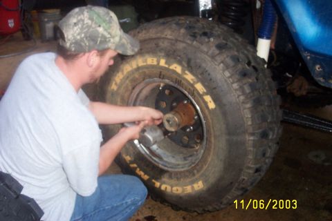 1979 Ford F-150 - A man uses an impact wrench to work on a large off-road tire mounted on a blue vehicle.