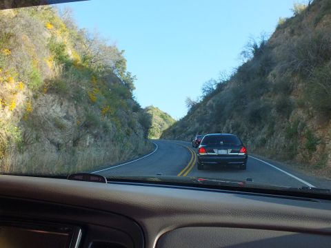 2003 Ford Crown Victoria - Windshield view of a black full-size sedan following a winding canyon road through green hills.