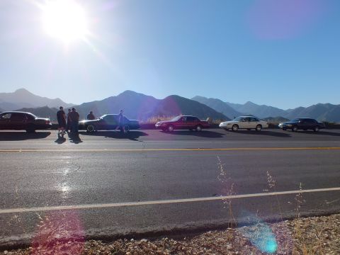 2003 Ford Crown Victoria - Group of sedans and an SUV parked along a mountain road, people standing as the sun sits low.