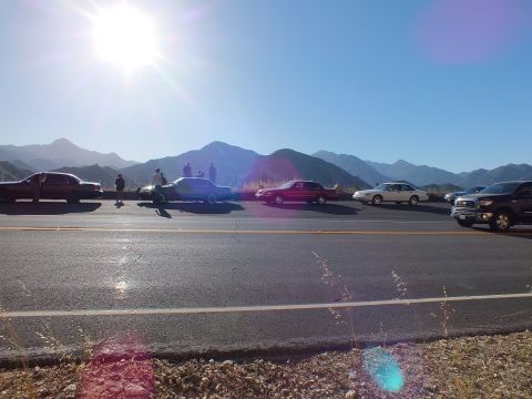 2003 Ford Crown Victoria - Cars and a pickup spread across a sunny roadside pullout, people gathered before mountain ridges.