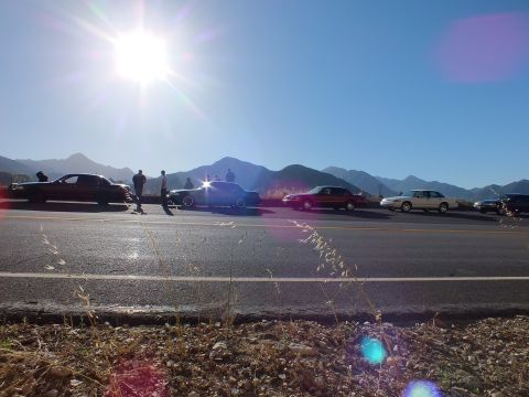 2003 Ford Crown Victoria - Row of full-size sedans and a person seated on a roof, backlit by sun over a mountain skyline.
