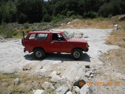 1986 Ford Bronco - This red 1986 Ford Bronco navigates a challenging rocky path, its off-road capabilities.