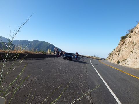 2003 Ford Crown Victoria - Onlookers cluster by a parked SUV on a cliffside turnout as the two-lane road bends along the mountainside.