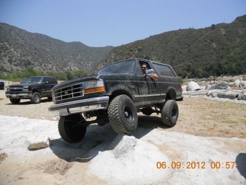 1986 Ford Bronco - A black Ford Bronco navigates rocky terrain, with a second truck in the background.