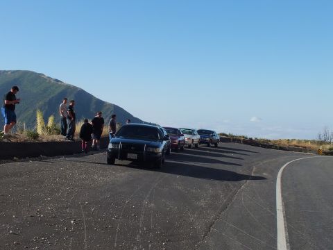 2003 Ford Crown Victoria - Dark sedan faces the camera at the head of a parked lineup; people stand at the overlook above the clouds.