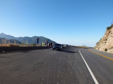 2003 Ford Crown Victoria - Parked SUV and onlookers on a wide overlook; the freshly paved road sweeps down the mountainside beyond.