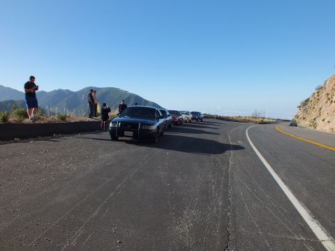 2003 Ford Crown Victoria - Dark Crown Victoria-style sedan at a cliffside pullout; people watch as the road curves down the ridge.