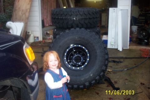 1979 Ford F-150 - A young child stands in front of large tires, with a dark vehicle partially visible on the left.