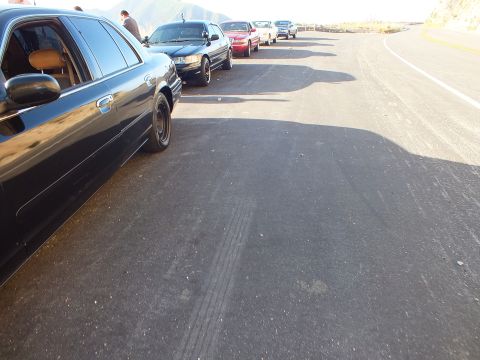 2003 Ford Crown Victoria - Low rear-quarter view down a line of parked cars on a ridge turnout; a red sedan and others sit ahead.