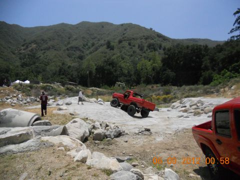 1986 Ford Bronco - A red off-road truck navigates a rocky terrain during an event.