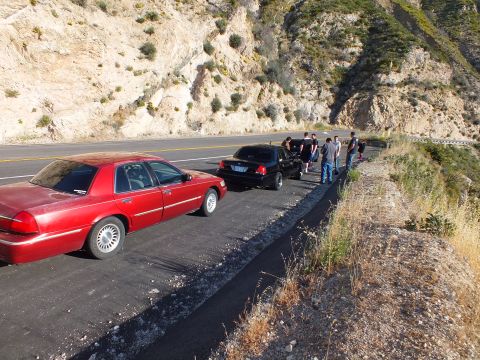 2003 Ford Crown Victoria - Red sedan parked behind a black one on a roadside; a group stands at the guardrail above the canyon.