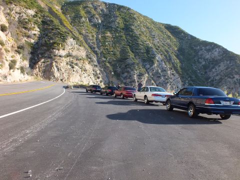 2003 Ford Crown Victoria - Five sedans parked single file on a wide paved shoulder beneath green hillsides