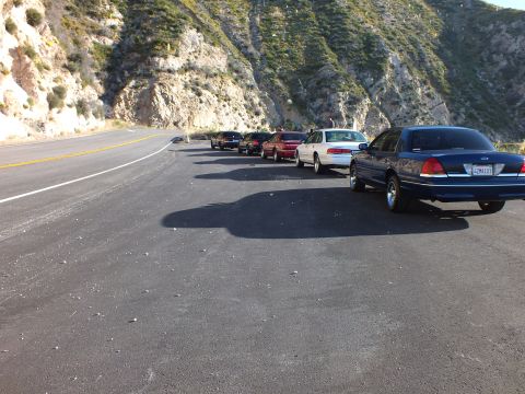 2003 Ford Crown Victoria - Sedans staged along a broad asphalt turnout with steep rocky canyon walls behind