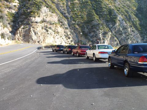 2003 Ford Crown Victoria - Multiple sedans queued on a mountain pullout, people gathered near the cars in afternoon light