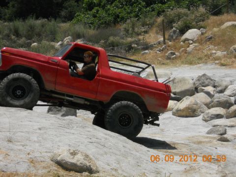 1986 Ford Bronco - A red off-road SUV navigates a rocky terrain.