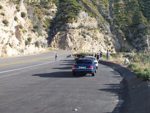 2003 Ford Crown Victoria - Blue sedan on a wide mountain road, a cyclist riding past and a group gathered at the guardrail