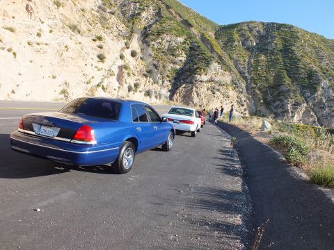 2003 Ford Crown Victoria - Blue sedan from behind on a mountain pullout, white car and people ahead near the guardrail