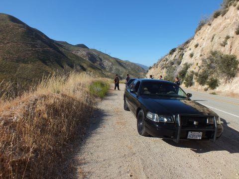 2003 Ford Crown Victoria - Black sedan with brush guard on a gravel pullout, people standing and green ridges beyond