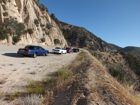 2003 Ford Crown Victoria - Several sedans pulled onto a wide dirt turnout, people standing between them above a brushy canyon