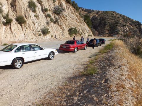 2003 Ford Crown Victoria - White full-size sedan parked first in a row of cars along a mountain highway pullout