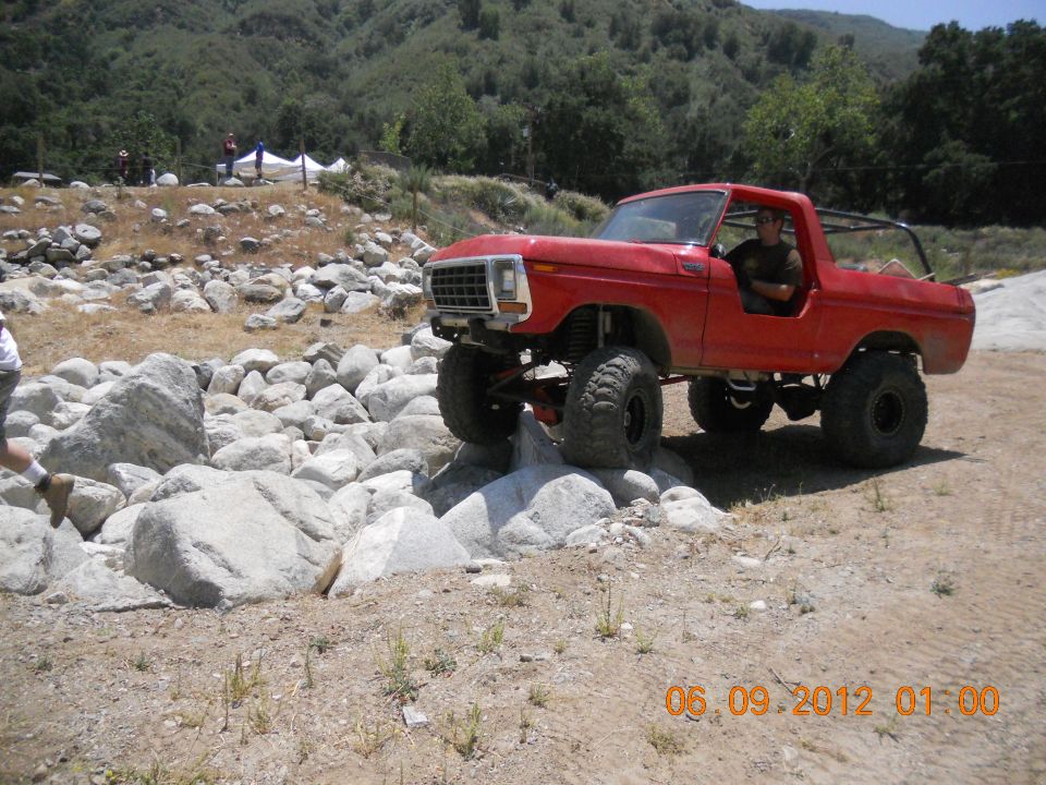 Red off-road SUV with lifted suspension and large tires navigating a rocky terrain
