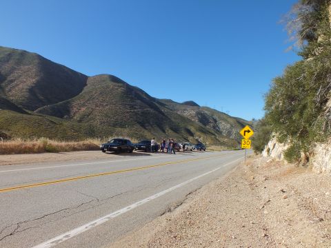 2003 Ford Crown Victoria - Wide view of a mountain highway with cars gathered on the opposite shoulder near a curve sign