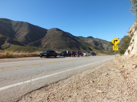 2003 Ford Crown Victoria - Group of cars and people on a mountain road turnout, sharp curve warning sign in the foreground