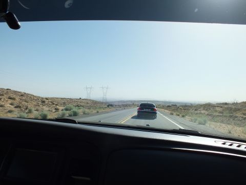 2003 Ford Crown Victoria - Following a sedan down an open desert highway, transmission towers on the horizon, shot from inside the car