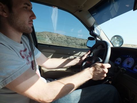 2003 Ford Crown Victoria - Driver at the wheel of a tan-interior car on a desert road, white-faced gauge cluster visible