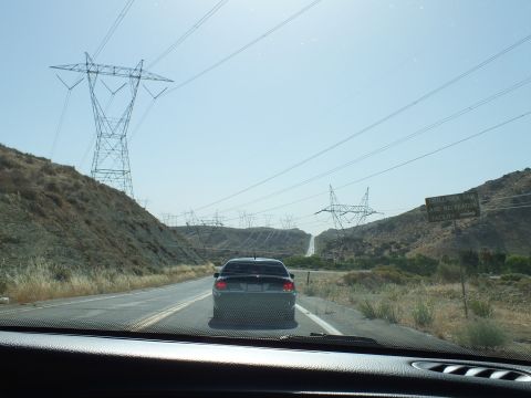 2003 Ford Crown Victoria - Windshield view of a sedan on a two-lane road below high-voltage towers, hillside warning sign at right