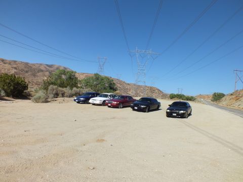 2003 Ford Crown Victoria - Wide view of sedans gathered in a sandy clearing below high-voltage towers and rocky hills