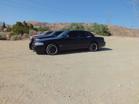 2003 Ford Crown Victoria - Side view of a blacked-out Panther-platform sedan on dark rims with other cars and power lines behind