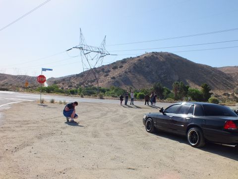 2003 Ford Crown Victoria - man squats beside a road sign as a black sedan and a transmission tower frame the dry junction