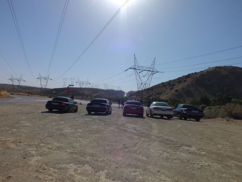 2003 Ford Crown Victoria - Mixed-color sedans line up on a dirt lot as sunlight floods the sky over transmission towers