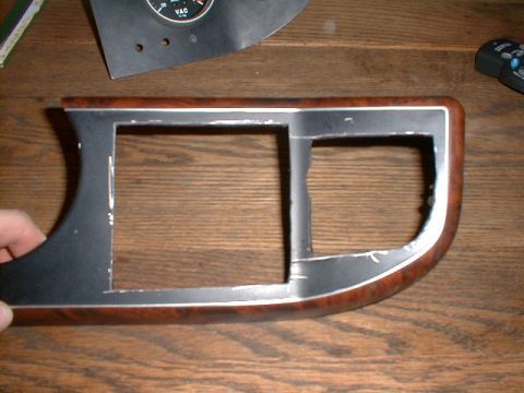 1990 Ford Bronco - Dashboard trim piece with a partial vacuum gauge. The trim has wood grain and chrome accents.