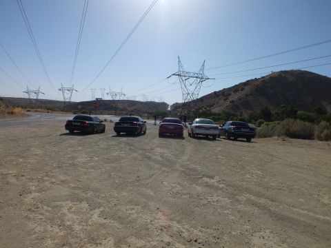 2003 Ford Crown Victoria - Five dark and silver sedans sit tail-out on a dirt lot under a network of transmission towers